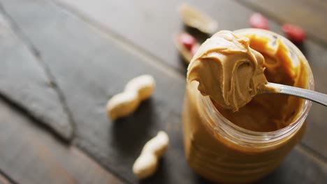 Video-of-close-up-of-peanut-butter-and-peanuts-on-wooden-background