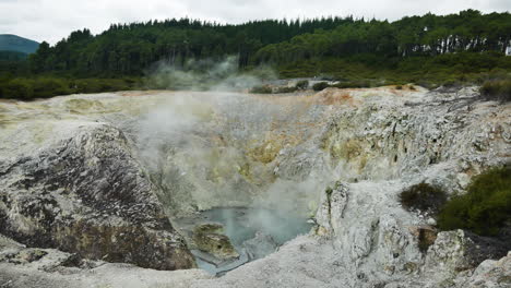 Wide-shot-of-small-geothermal-water-pool-boiling-and-steam-rising-up-to-sky---Wai-o-Tapu,New-Zealand