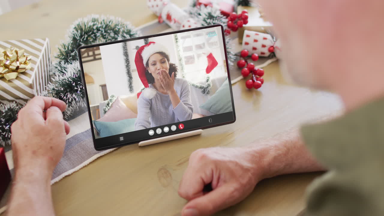 hombre caucásico con decoraciones navideñas teniendo una llamada de video de tableta con una mujer biracial