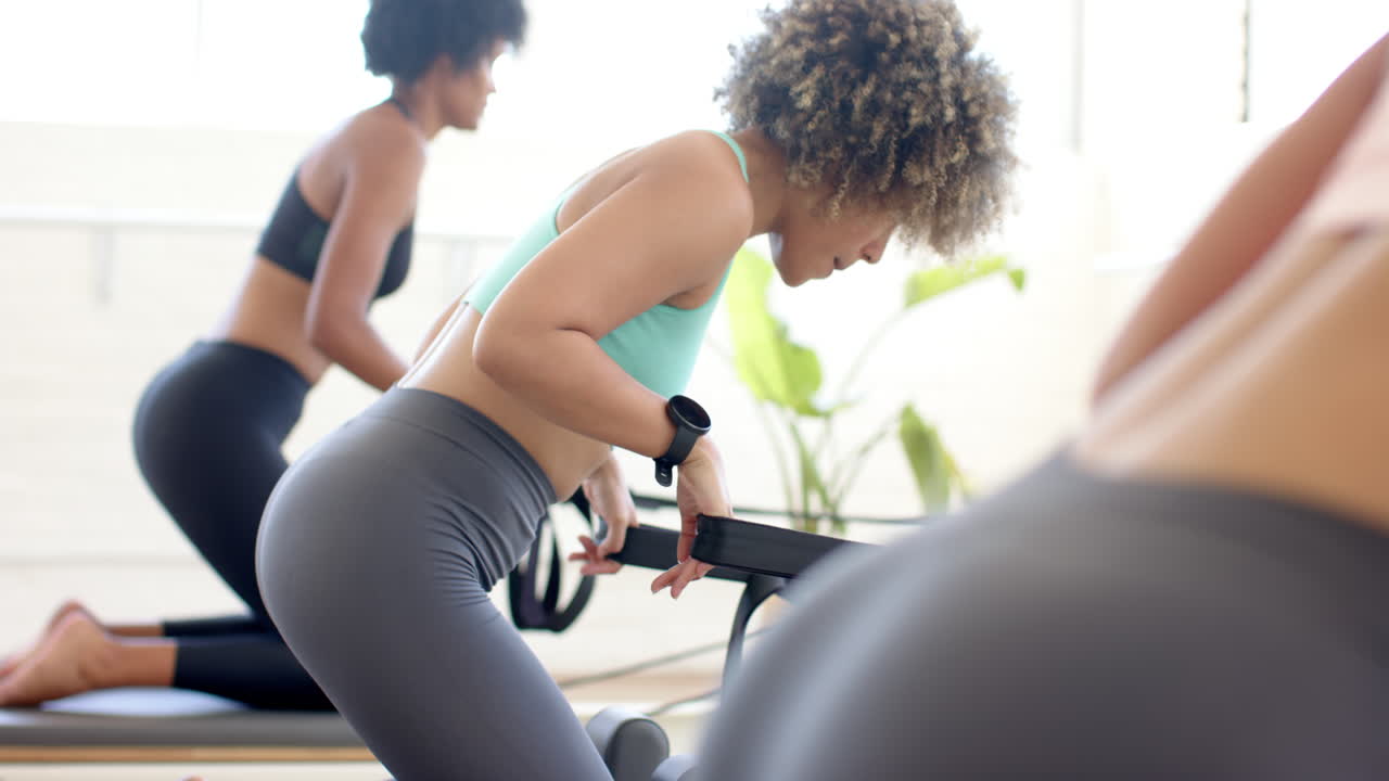 mujer biracial ajustando la tableta durante la clase de yoga, amigos diversos practicando