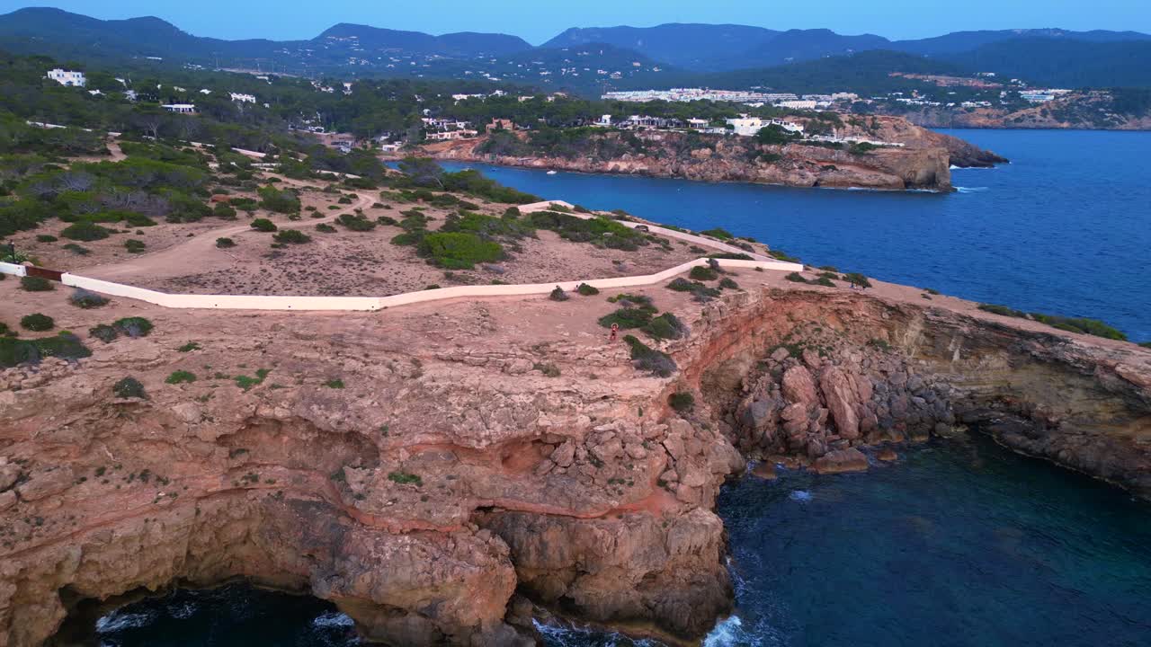 Donna che esegue la posizione dell'albero yoga su una scogliera rocciosa durante un sereno tramonto a Ibiza. Bella vista aerea, volo, flycam, panorama inverso, orbit, drone