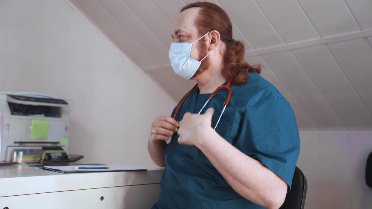 Infermiera bianca che prepara lo stetoscopio per un teleconsulto nell'ufficio di casa, sistema mascherina ed elastici per le orecchie, seduta accanto a stampante e documenti, concentrata sulla connessione virtuale con il paziente, con una presenza professionale calma