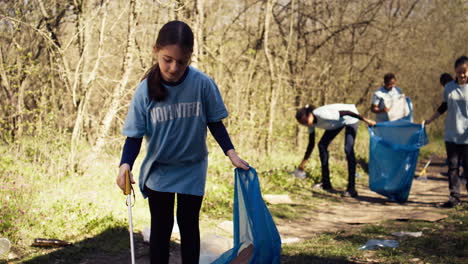 young child using tongs tool to grab and pick up trash from the woods