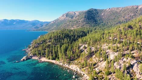 exuberantes montañas y bosques de pinos en el lago tahoe, california con agua azul cristalina y playa con embarcadero de roca - toma aérea de drones