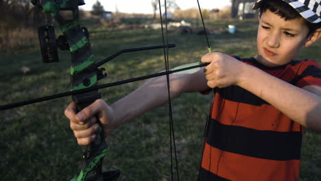 young sporty boy aiming bow arrow in the field