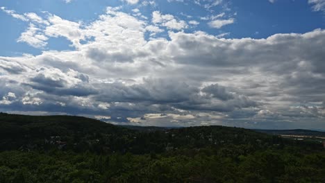 time lapse of a dramatic sky filled with thick clouds stretches above a landscape of lush green hills and scattered homes. the sunlight filters faintly through the clouds