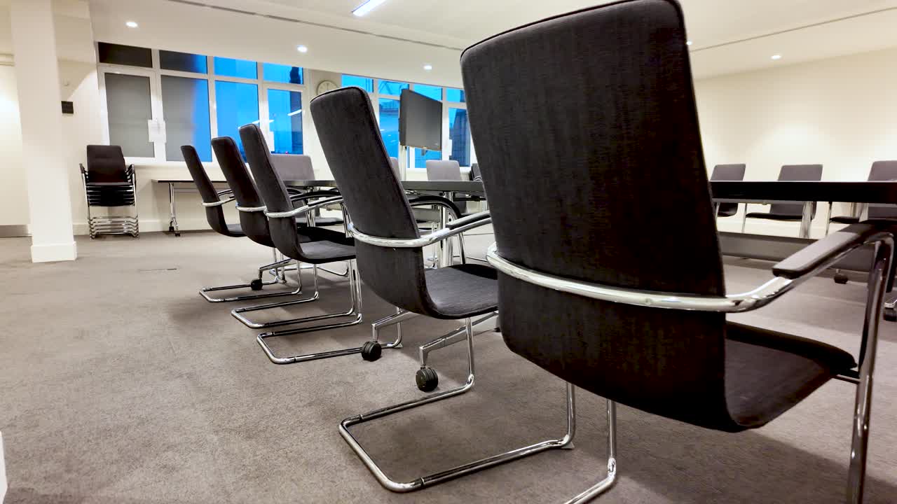 Interior moderno de sala de juntas corporativa con sillas de cuero negro en fila, mesa de conferencias y luz natural de las ventanas para reuniones de negocios y presentaciones