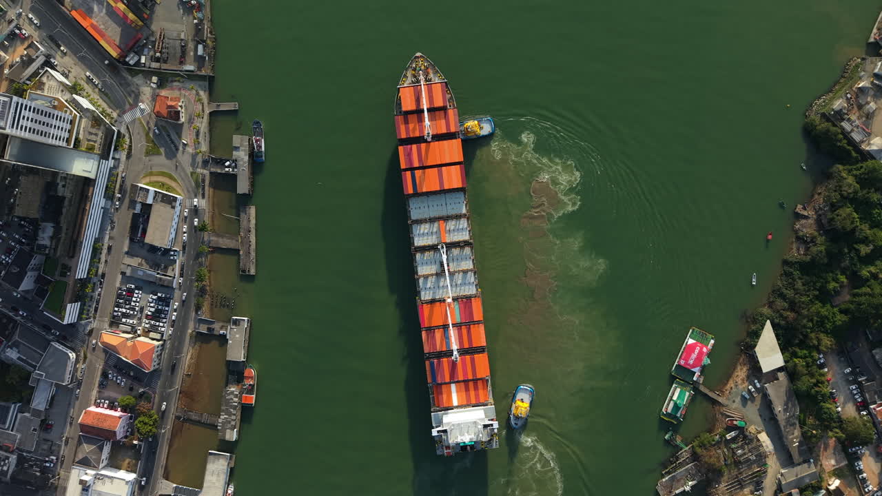 Aerial tops down above colorful Container Ship, transportation cargo in green waters of Itajaí port, Brazil