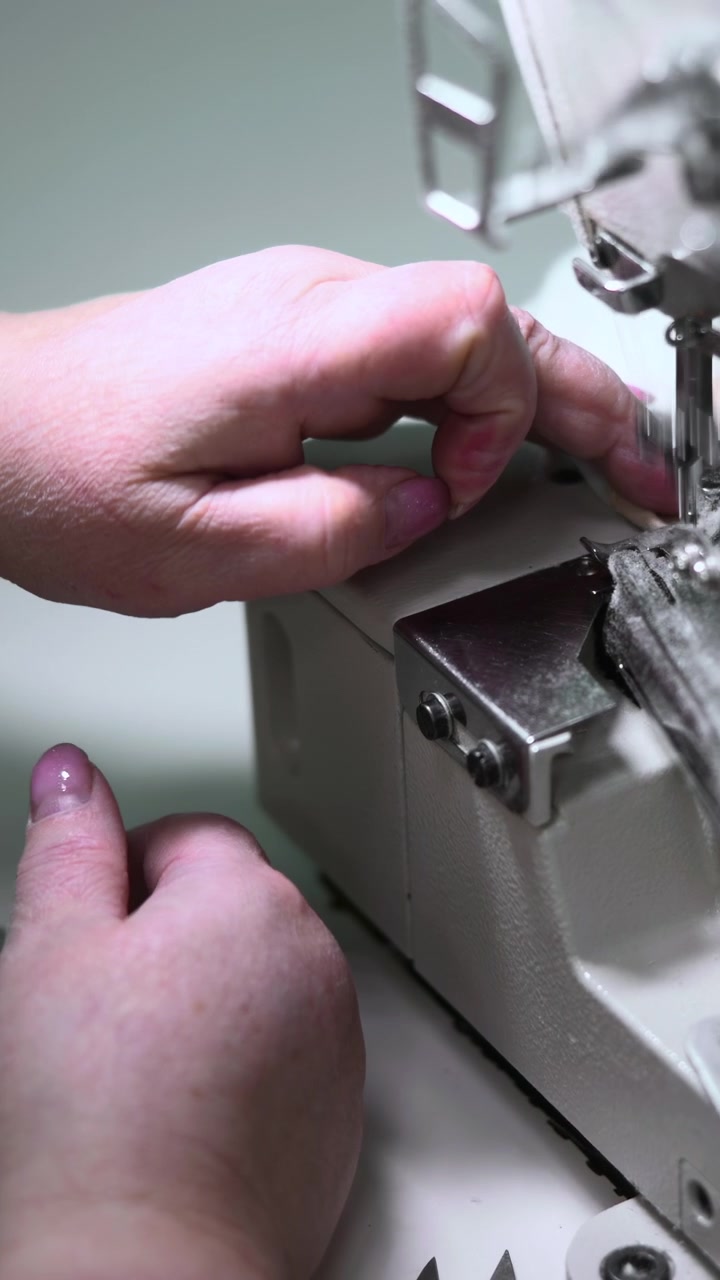 Costureira em Fábrica Branca Operando Máquina Overlock em Costura, Mãos em Close-up Guiando a Borda Através de uma Overlock Rápida.