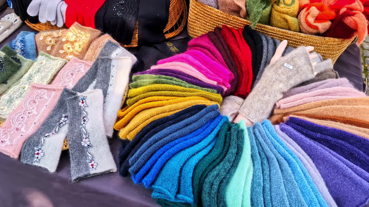 Guanti, sciarpe e accessori in maglia fatti a mano e colorati esposti ordinatamente presso una bancarella di un mercato artigianale locale, che mostrano una vivace moda invernale.