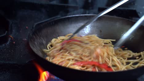 chef experto cocinando espagueti salteado, sazonado con sal y pimienta, volviendo y agitando hábilmente los ingredientes en una sartén chisporroteante, el humo aromático llena la atmósfera de una cocina comercial