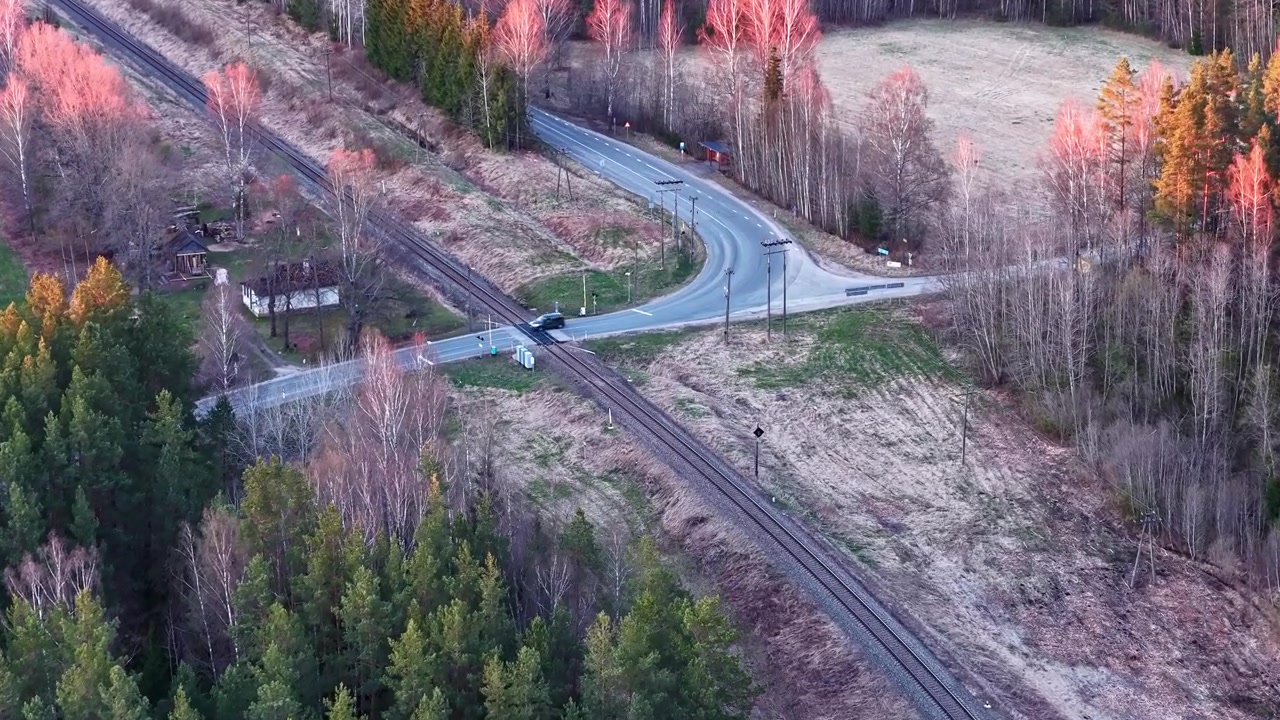 Bil nærmer sig en jernbaneoverskæring og et landligt vejkryds under en smuk solnedgang om foråret.