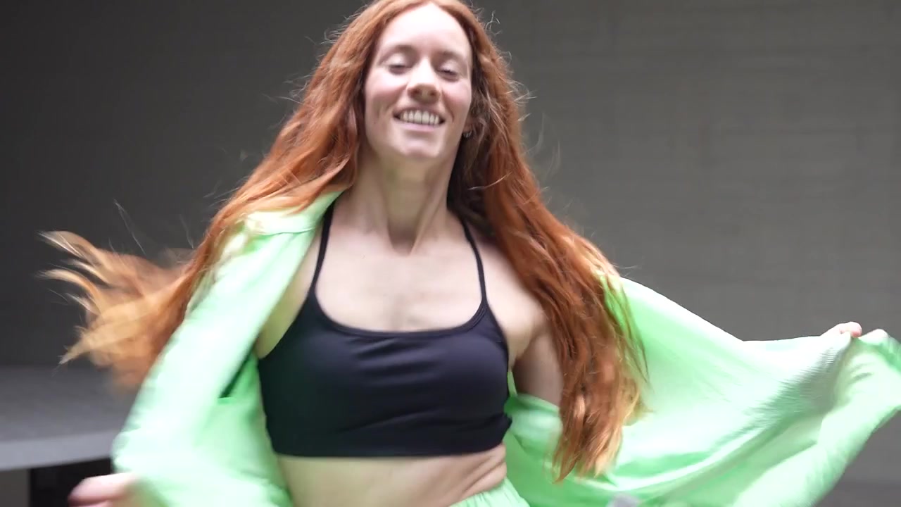 En dynamisk kvinde danser i neongrønt under farverige lys, der udstråler energi og entusiasme.