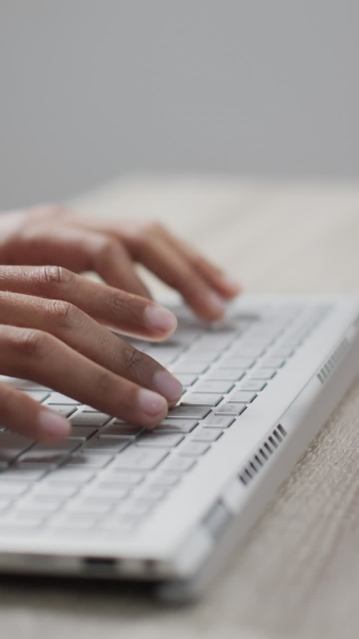 Vertical video of biracial businessman using laptop on grey background
