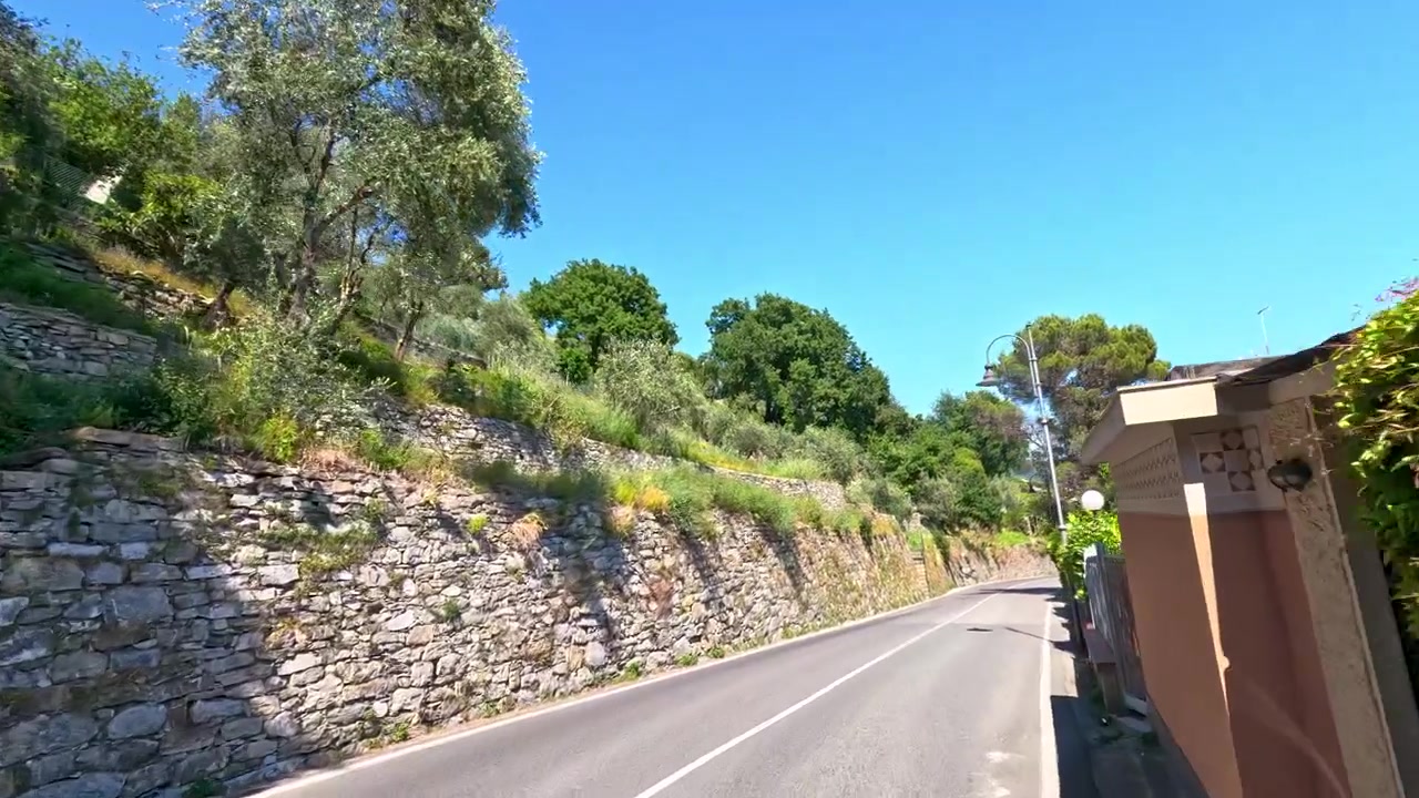 Un'inquadratura fluida della telecamera in movimento in avanti segue una strada asfaltata attraverso colline mediterranee soleggiate e vegetazione