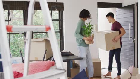 Happy-diverse-male-couple-moving-house,-carrying-boxes-and-smiling
