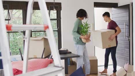 happy diverse male couple moving house, carrying boxes and smiling