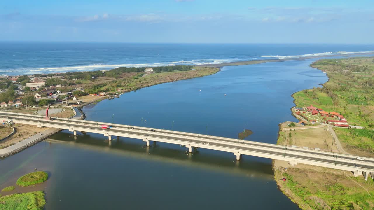 Aerial view of a bridge that crosses the river estuary with coastline and blue sky horizon on the background. Kretek II bridge, Depok Beach, Yogyakarta, Indonesia. 4K Indonesia landmark drone video.