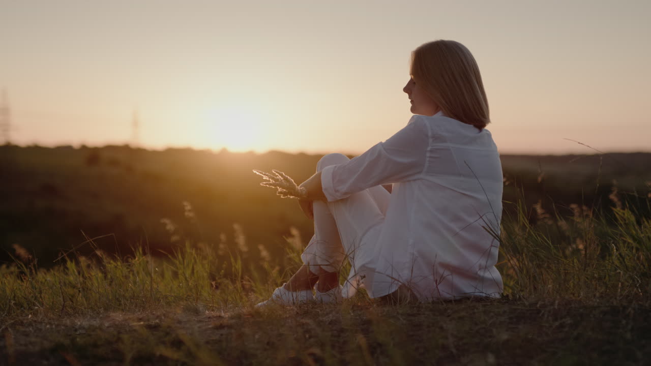 하얀 양복을 입은 여자가 석양을 감상하는 언덕에 앉아 1