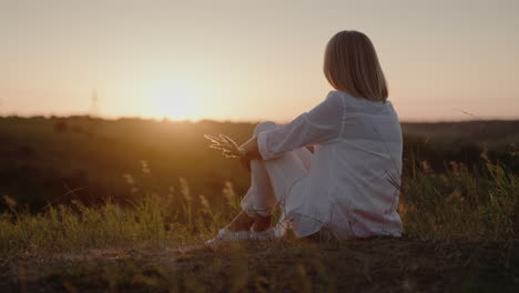 Una-Mujer-Con-Un-Traje-Blanco-Se-Sienta-En-Una-Colina-Admirando-La-Puesta-De-Sol-1