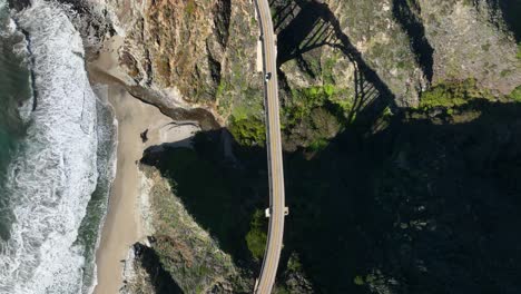 top down view following car along highway 1 coastline, waves and seashore below, bixby bridge big sur, california