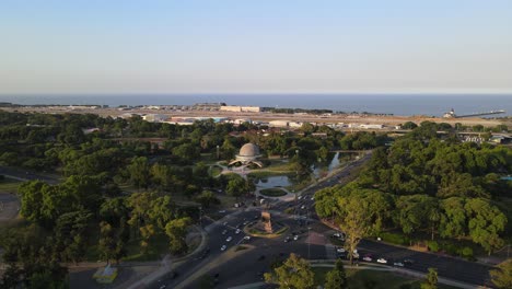 Dolly-in-of-Monumento-to-the-Spanish-and-Palermo-woods-leading-to-Galileo-Galilei-Planetarium-with-Rio-de-la-Plata-river-in-background,-Buenos-Aires,-Argentina