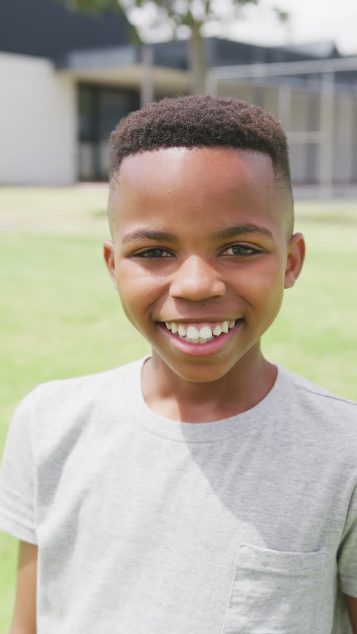 Vertical video portrait of happy african american schoolboy smiling in schoolyard, copy space