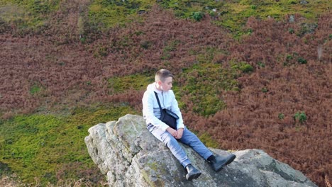 aerial footage revolves around a thoughtful young boy seated on a substantial rock outcrop in the midst of the moorland