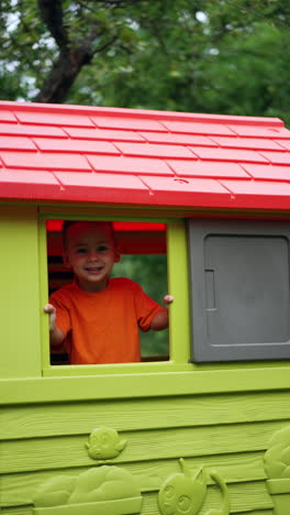 cute baby boy looks out of a window of a plastic playhouse. lovely kid laughs happily. vertical video.