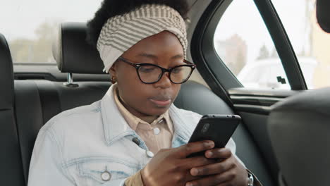 african american woman messaging on phone in car