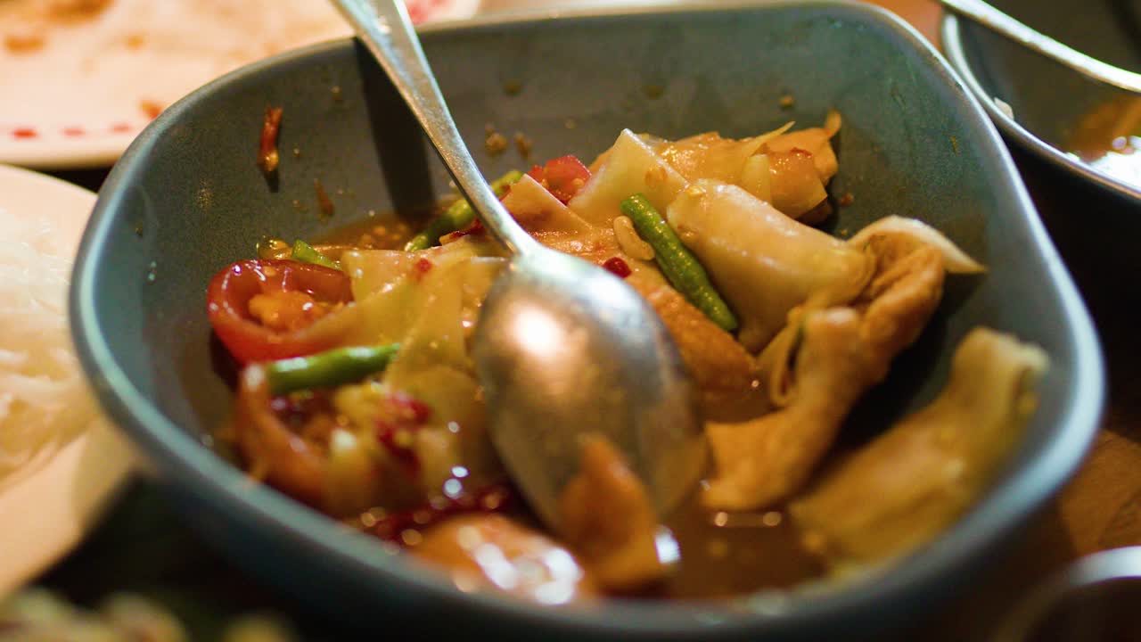 Close-up of som tam papaya salad with green beans, tomatoes, and dressing in natural light