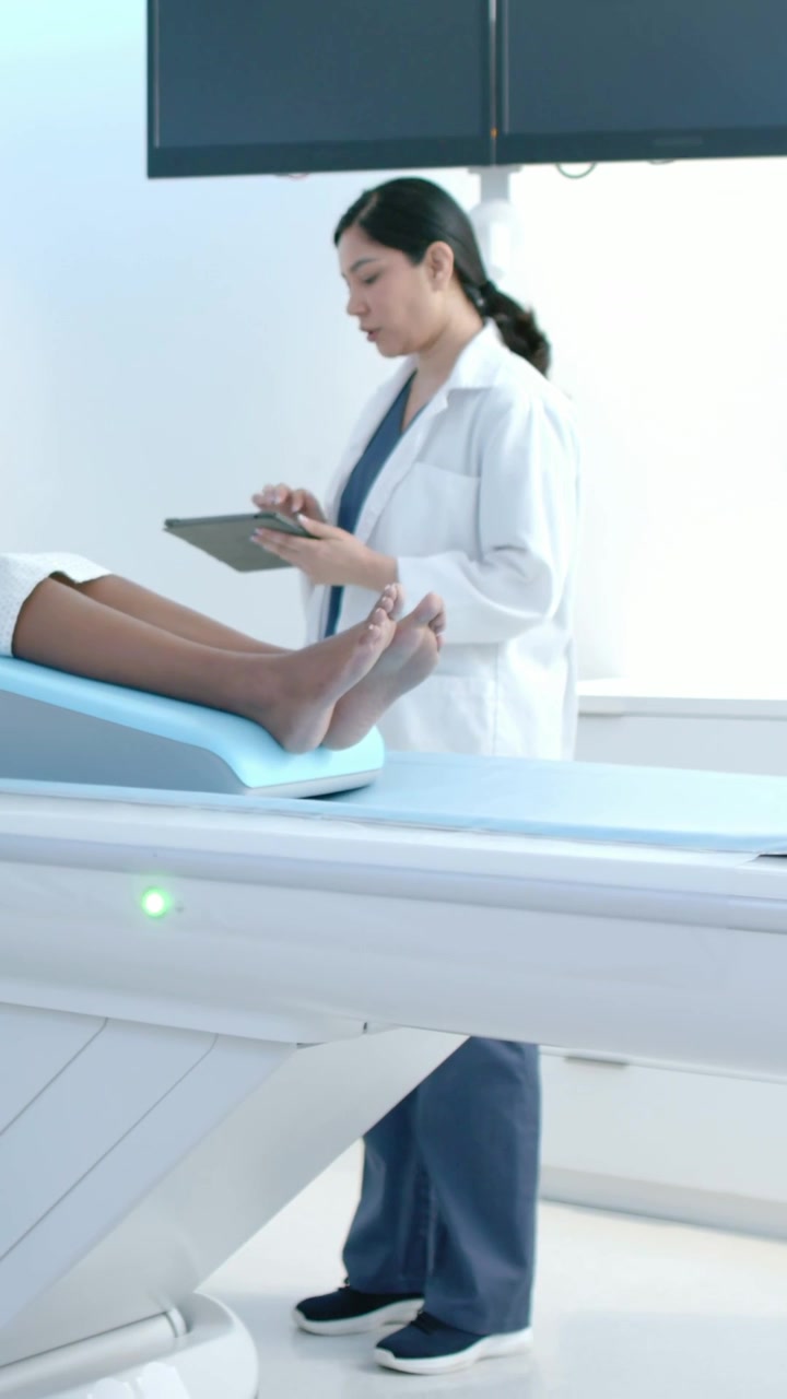 Vertical video: Noticing green light, tech in lab coat tapping tablet at scanner, checking settings