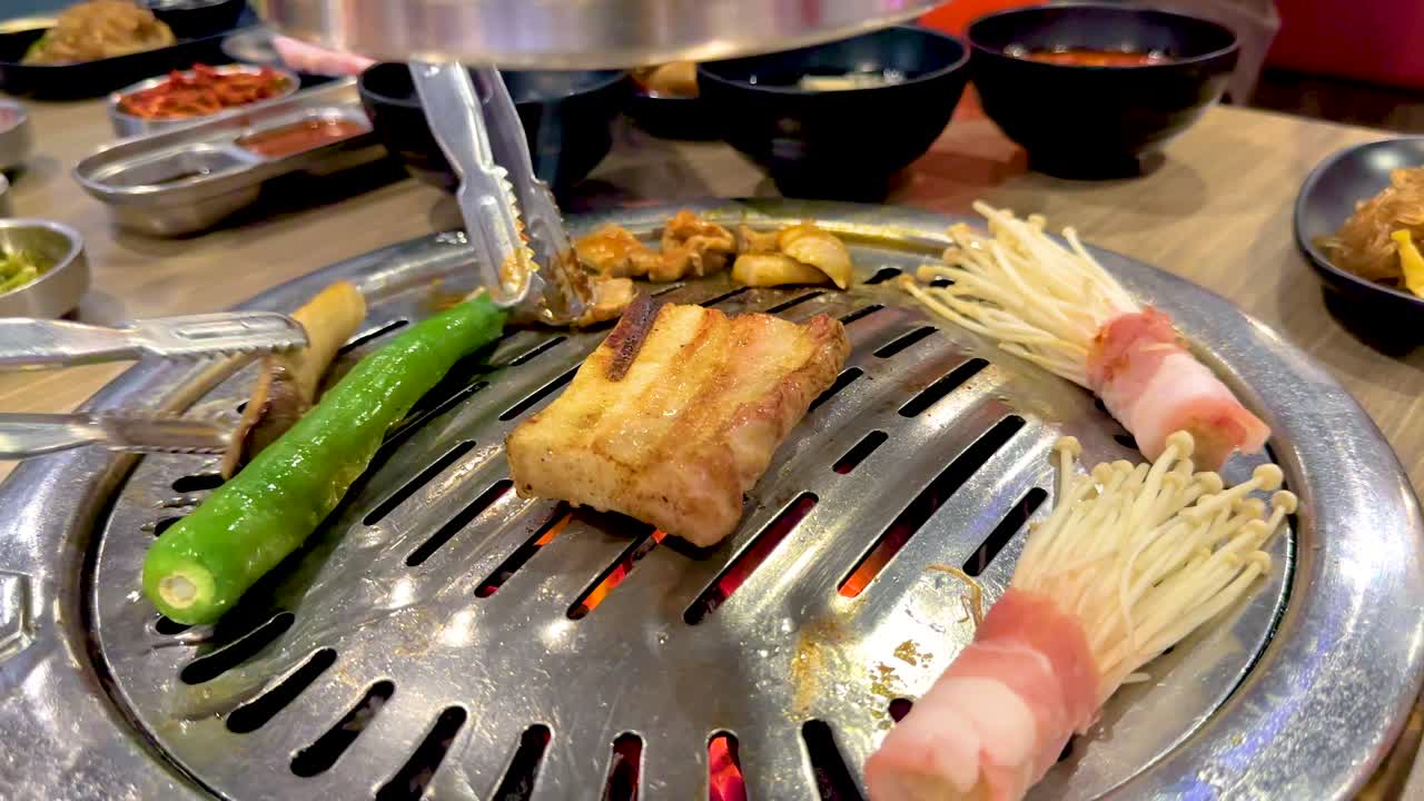 Grilled meats and vegetables sizzle on a tabletop BBQ grill in a vibrant Bangkok setting, capturing the essence of Korean cuisine