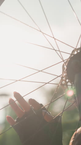 primer plano de un adulto joven tocando suavemente la rueda de la bicicleta mientras la luz del sol se refleja en ella, la rueda gira lentamente, y ella aparece ligeramente borrosa, en un fondo de vegetación vibrante