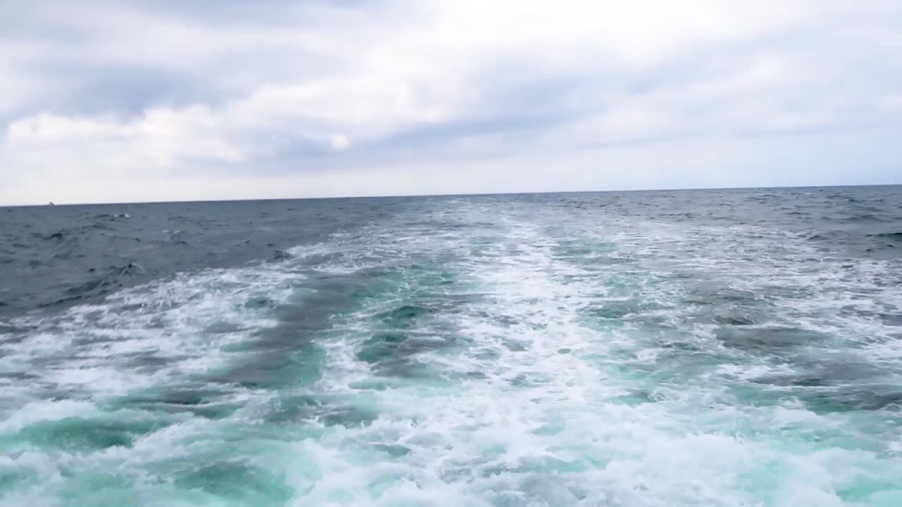 Boat traveling the pacific ocean watching the waves splash in the rear of the boat.