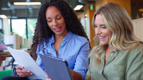 businesswomen with digital tablet having informal meeting in breakout seating area of modern office