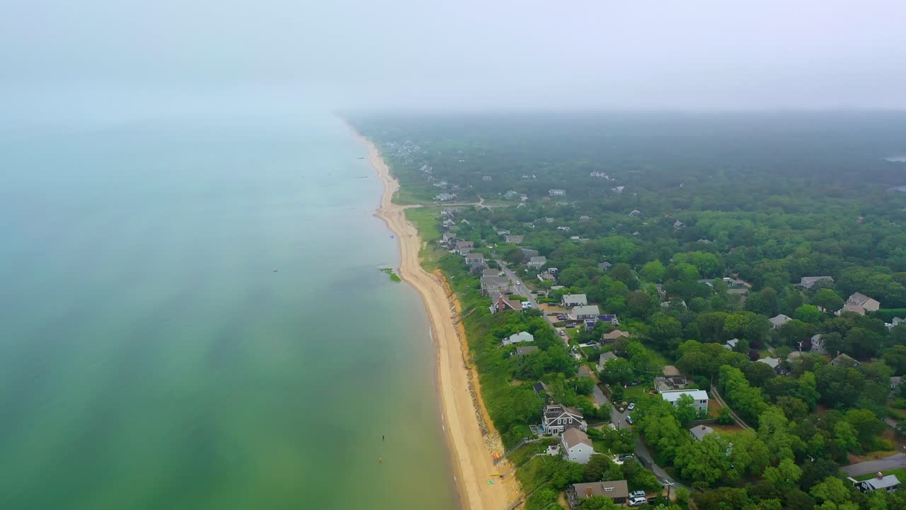 Panorama aereo con drone della costa di Cape Cod con cielo nebbioso, case sull'oceano, spiagge sabbiose e quartieri costieri che sfumano nella nebbia oltre il rigoglioso paesaggio ricco di alberi