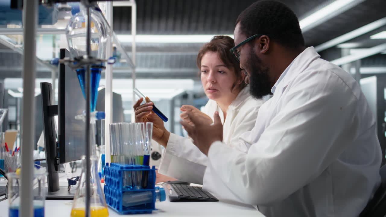 Vertical video Teamworking lab technicians inspect liquids in glass flasks