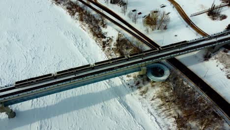 Aerial-winter-dolly-roll-birds-eye-view-from-vintage-historic-high-level-bridge-to-the-public-transit-train-bridge-of-Dudley-B-Menzies-while-5-accordian-trains-cross-from-downtown-to-uptown-Whyte-Ave