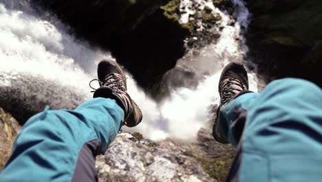 person sitting above a beautiful waterfall, slow motion shot at day time of hiker in norway, europe