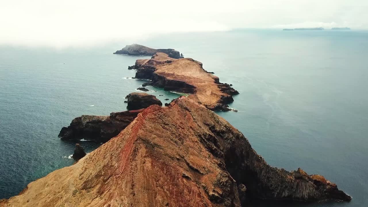 Aerial view of the rugged coastal peninsula of Ponta de São Lourenço, Madeira, featuring striking cliffs, arid terrain, and the surrounding expansive blue Atlantic Ocean under a lightly clouded sky