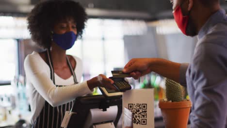 mixed race man giving african american female cafe worker his credit card in order to pay