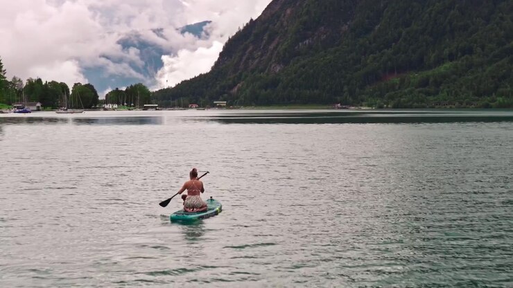 Vista di tracciamento con drone di una donna in paddleboard sul Lago Achensee, paesaggio alpino austriaco.