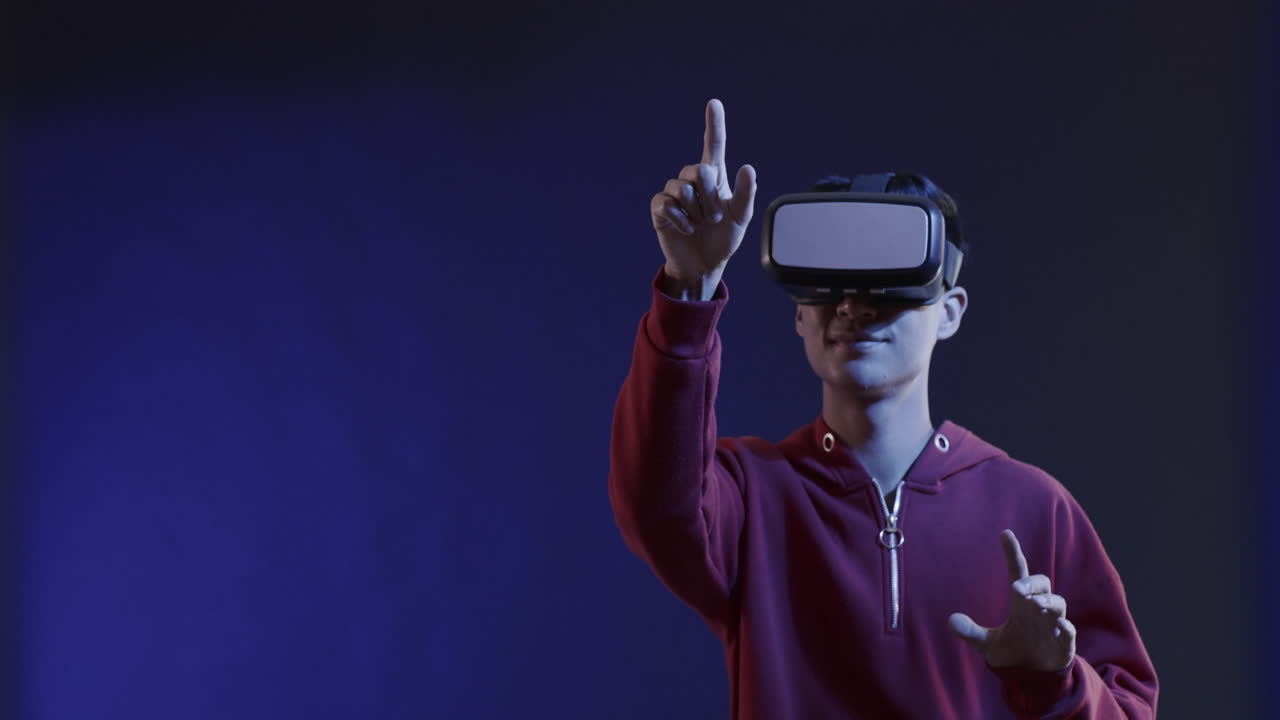 Asian man using vr headset, touching virtual screen on blue background, copy space, slow motion