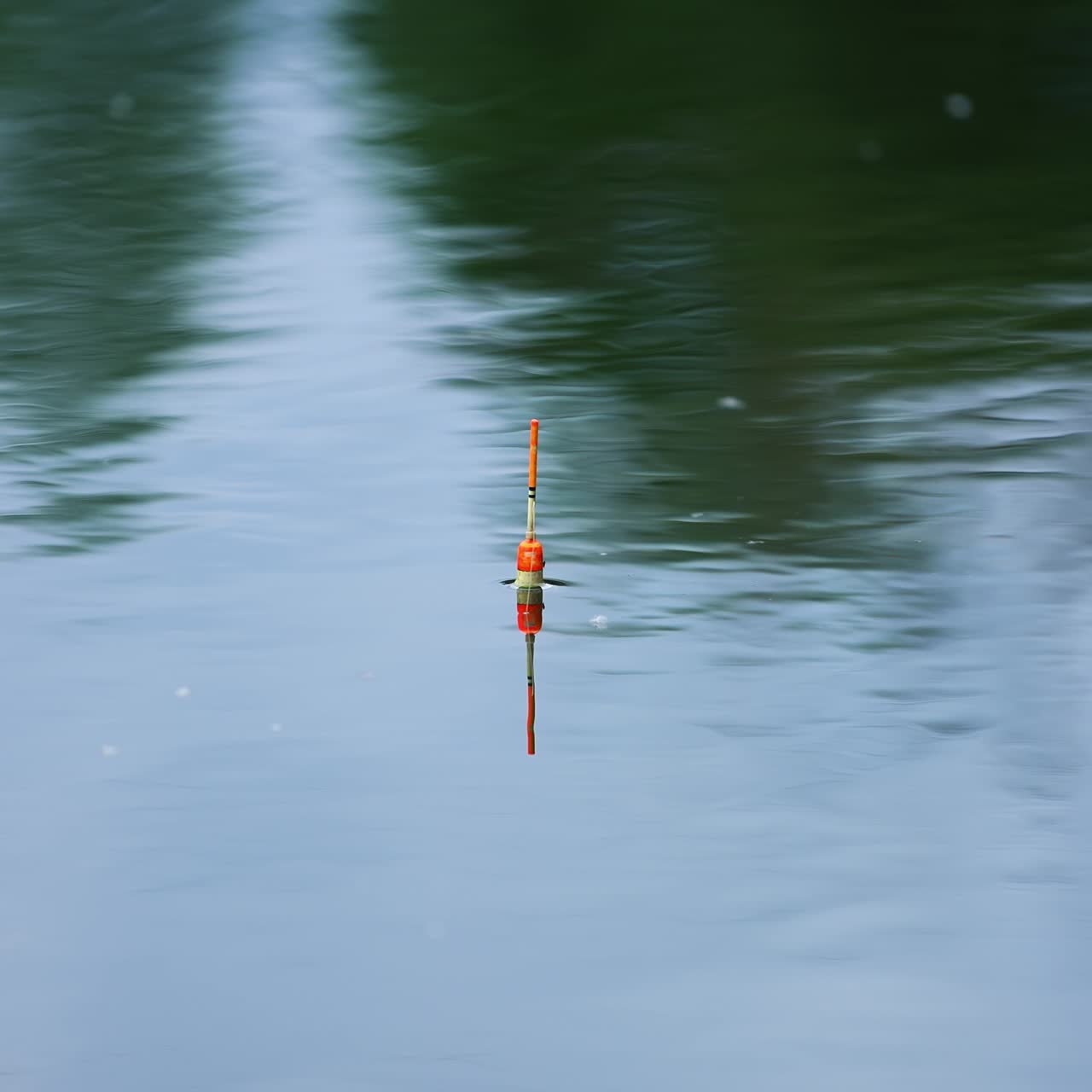 White and orange fishing bobber floating in the river. Unmoving float on still water on cloudy day