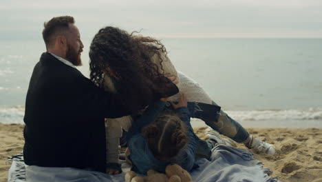 Family-laughing-enjoying-beach-together-on-sea-vacation.-Parents-tickle-child.