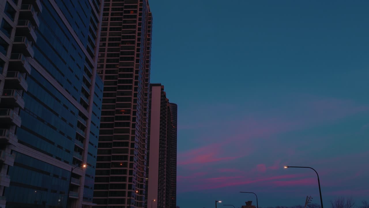 Grandes edificios bordean la calle mientras el crepúsculo cae en Chicago, con las farolas comenzando a brillar. Captura la transición del día a la noche, ideal para narrativas urbanas.
