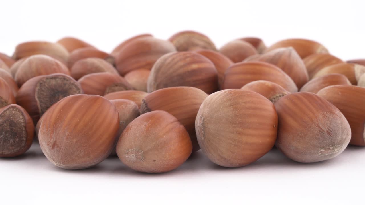 A pile of round, shelled hazelnuts smoothly rotating on the turntable, isolated on the white background. Close-up. Macro.