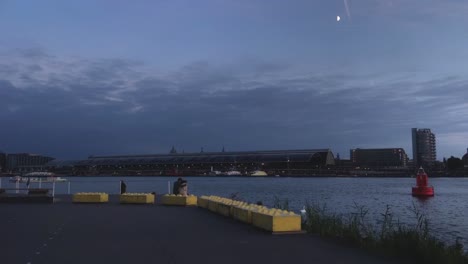 the ij in blue moonlight, the silhouette of a couple sitting at the water in front of the amsterdam central station