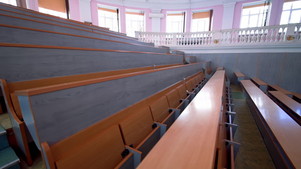 Rows of long desks in conference hall. Empty auditorium in the modern educational center. Wooden tables without students in large comfortable classroom.